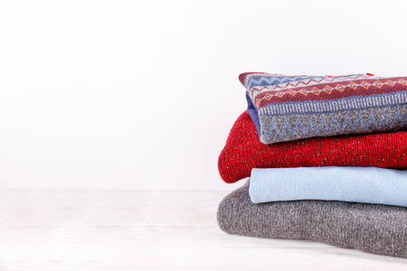 Bunch of colorful sweaters with different patterns stacked in messy pile on white wooden table,...