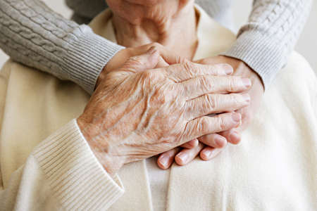 Mature female in elderly care facility gets help from hospital personnel nurse. Senior woman, aged wrinkled skin & hands of her care giver. Grand mother everyday life. Background, copy space, close upの写真素材