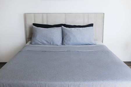 Hotel room with freshly made king sized bed with headboard, perfectly clean and ironed sheets, puffy pillows in natural sun light. Kingsize bed in a furniture showroom. Close up, copy space for text.の写真素材
