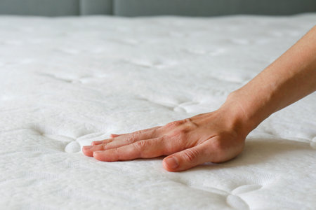Cropped shot of man testing the firmness of white orthopedic mattress. Male pressing hypoallergenic foam mattresses surface to check its softness. Close up, copy space, top view, background.の写真素材