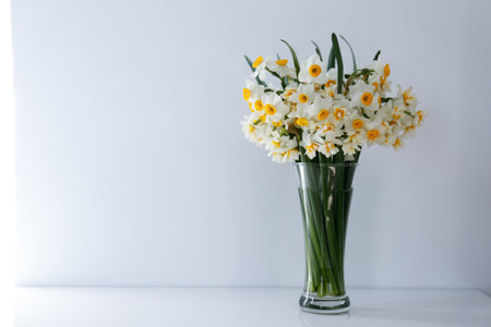 A bouquet of white daffodils in glass vase on the table, natural sunlight. Narcissus flowers in minimal close up composition with visible petal texture. Background, copy space top view.の写真素材