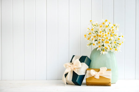Lush bouquet of white-yellow daffodils in vintage turquoise vase and presents, wooden plank wall background. Tender minimalistic spring flowers composition. Top view, copy space, flat lay, close up.の写真素材