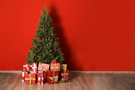 Decorated Christmas tree with gifts in room on color wall backgroundの写真素材
