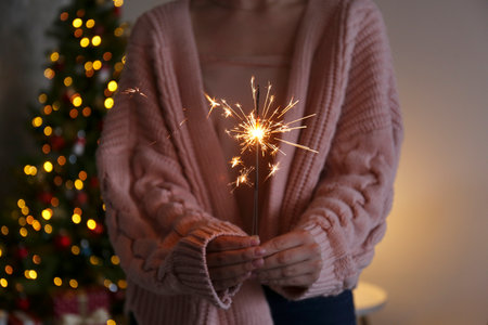 Woman holding burning sparkler in front of Christmas tree, closeupの写真素材