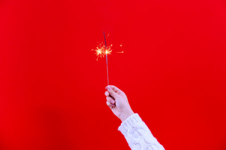 Woman hand holding sparkler on red background. Christmas and New Year conceptの写真素材