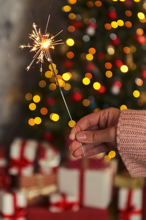 Female hand with sparkler and Christmas gifts on blurred background, closeupの写真素材