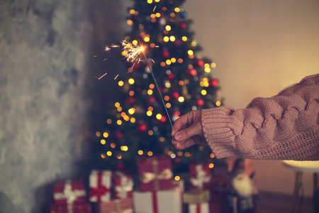 Woman holding sparkler in hands on background of Christmas tree and giftsの写真素材