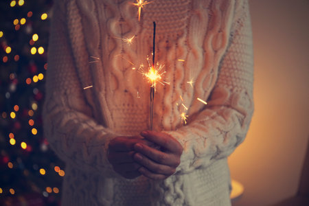 Woman holding a sparkler in her hands on the background of a Christmas treeの写真素材