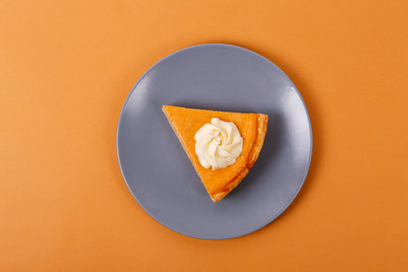 Slice of pumpkin pie with whipped cream on blue plate on orange backgroundの写真素材