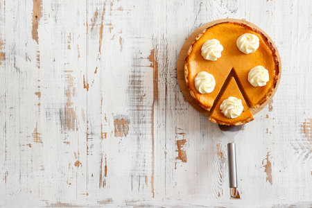 Piece of pumpkin pie with whipped cream on white wooden background.の写真素材