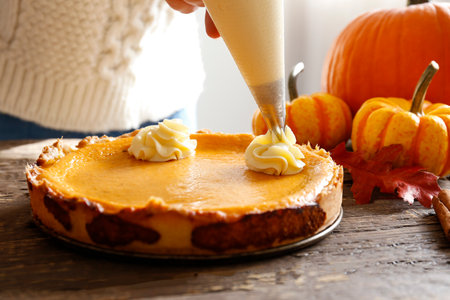 Woman decorating pumpkin pie with whipped cream on wooden table, closeupの写真素材