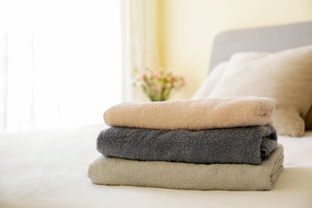 Hotel room with freshly made bed, perfectly clean and ironed sheets, stack of new folded towels in natural sun light. Close up, copy space for text.の写真素材
