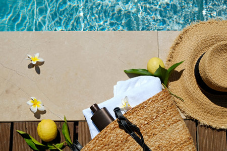 Swimming pool essentials concept. Beach bag with items for safe sunbathing on the deck, sunglasses,...