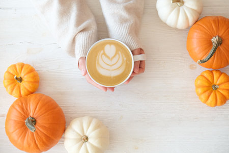 Hands holding cup of coffee with pumpkins on white wooden backgroundの写真素材