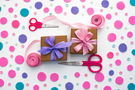 Two holiday gift boxes are tied with satin ribbon on background with colorful confetti. Top view of...