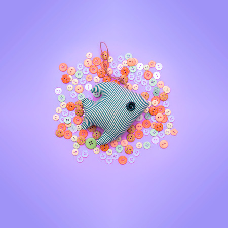 Textile toy fish on the background of the buttons. Common gentle purple background. Top view Flat Layの写真素材
