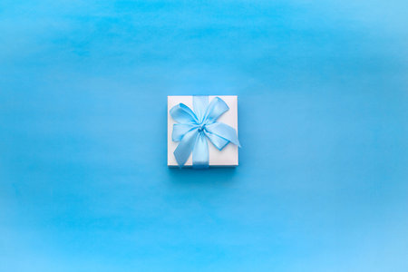 Gift box decorated with a satin ribbon on a blue background. View from above