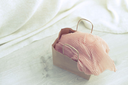 A paper bag with purchases on the wooden light background. Light pink scarf in a paper bag Gift to a woman. Flat lay fashion accessoriesの写真素材