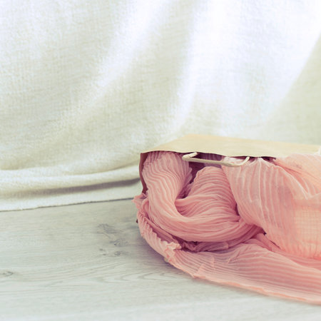 A paper bag with purchases on the wooden light background. Light pink scarf in a paper bag Gift to a woman. Flat lay fashion accessoriesの写真素材