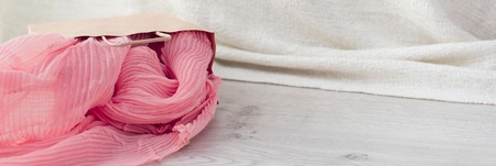 Banner A paper bag with purchases on the wooden light background. Light pink scarf in a paper bag Gift to a woman. Flat lay fashion accessoriesの写真素材