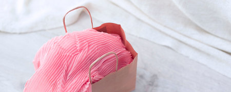 Banner A paper bag with purchases on the wooden light background. Light pink scarf in a paper bag Gift to a woman. Flat lay fashion accessoriesの写真素材