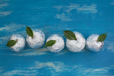 Five apples in the shell foil with natural green leaves. Wooden candy blue background. Flat lay top viewの写真素材