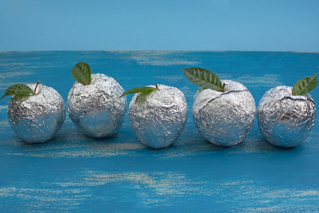 Five apples in the shell foil with natural green leaves. Wooden candy blue background. Flat lay top viewの写真素材