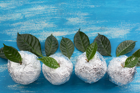 Four apples in the shell foil with natural green leaves. Wooden candy blue background. Flat lay top viewの写真素材