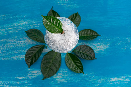 One Apple on blue shabby background in foil wrapped green leaves. The view from the topの写真素材
