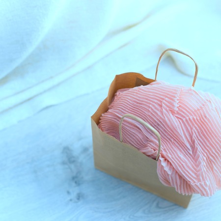 Toning A paper bag with purchases on the wooden light background. Light pink scarf in a paper bag Gift to a woman. Flat lay fashion accessoriesの写真素材