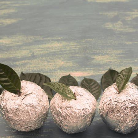 Three apples wrapped in foil are natural green leaves. Wooden candy blue background. Flat lay top viewの写真素材