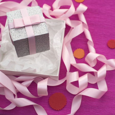 Festive composition with gift box on a bright pink background. Decoration satin ribbon bow. Textured backgroundの写真素材