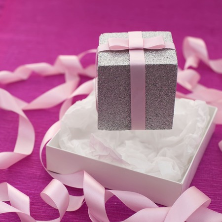 Festive composition with gift box on a bright pink background. Decoration satin ribbon bow. Textured backgroundの写真素材