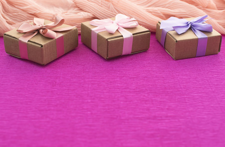 Festive composition three Kraft boxes with gifts on bright pink background. Decoration satin ribbon bow. Textured backgroundの写真素材