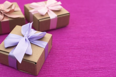 Festive composition three Kraft boxes with gifts on bright pink background. Decoration satin ribbon bow. Textured backgroundの写真素材