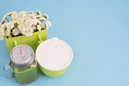 Glass mug with a tube with fresh smoothies.Container with porridge for Breakfast or lunch. Dining soup natural chrysanthemum flowers on blue background flat layの写真素材