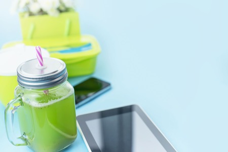 Glass mug with a tube with fresh smoothies. Smartphone natural chrysanthemum flowers on blue backgroundの写真素材