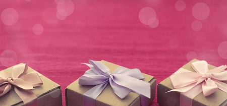 Banner Festive composition three Kraft boxes with gifts on bright pink background. Decoration satin ribbon bow. Textured backgroundの写真素材