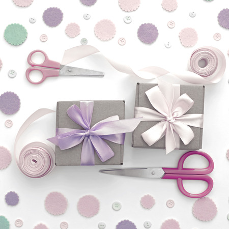 Two gift boxes on festive pastel confetti background. Wrapping gifts in Kraft boxes with a satin ribbon bow scissors. Flat lay top viewの写真素材