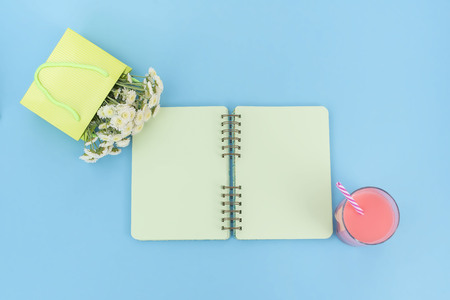 Open notebook for records lies on the surface of the cocktail pink glass tube bouquet of chrysanthemums. The pastel blue background copy spaceの写真素材