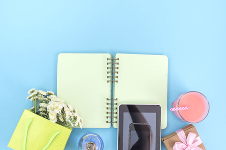 The opened notebook for records lies on the surface of the cocktail pink glass tube bouquet chrysanthemum perfume tablet box gift telephone. The pastel blue background copy spaceの写真素材