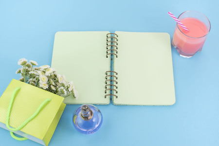 Open notebook for records lies on the surface of the cocktail pink glass tube bouquet of chrysanthemums perfume. The pastel blue background copy spaceの写真素材