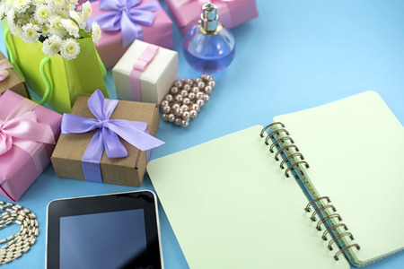 Festive background poster box gift satin ribbon bow bouquet of flowers jewelry pearl notebook tablet smartphone background blue. Top view copy space flat layの写真素材