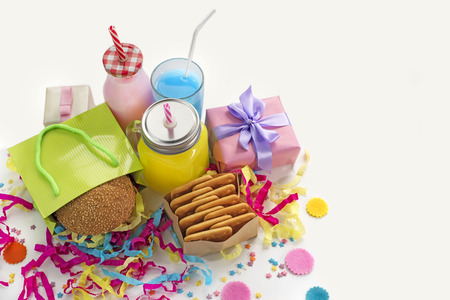 Festive composition of drinks, snacks, holiday hamburger, cookie, tinsel, confetti, gift box, cocktail and saturated colors. Children's holiday birthday partyの写真素材