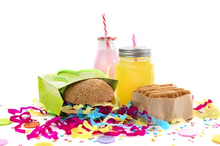 Festive composition of drinks, snacks, holiday hamburger, cookie, tinsel, confetti, gift box, cocktail and saturated colors. Children's holiday birthday partyの写真素材