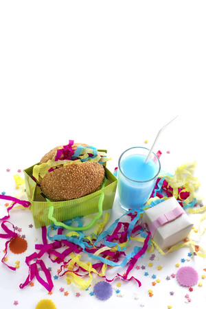 Festive composition of drinks, snacks, holiday hamburger, cookie, tinsel, confetti, gift box, cocktail and saturated colors. Children's holiday birthday partyの写真素材