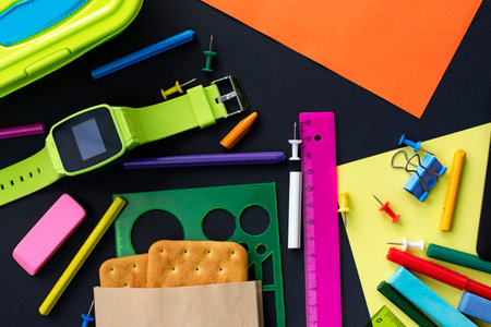 Concept back to school of watch, chalk, line, cookies and stationery on black background. Top view...