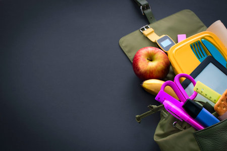 Backpack with school supplies on black background. Top view Flat lay