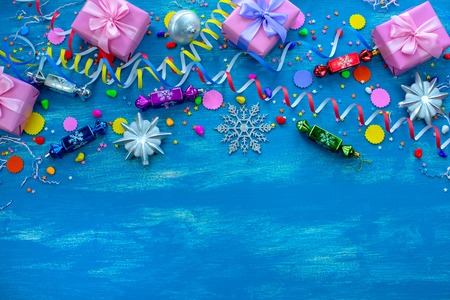Festive bright blue background decoration for holiday colored confetti serpentine paper gifts. Top view flat lay copy space Christmas candy snowflakes toysの写真素材