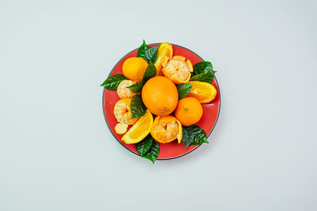 Red plate of oranges and tangerines with green leaves on a light background Top view copy spaceの写真素材